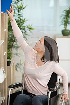 woman in wheelchair reaching for book from high shelf