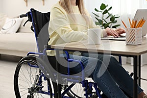Woman in wheelchair using laptop at home, closeup