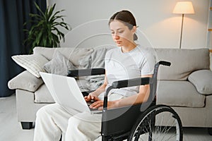 woman in a wheelchair works on the laptop PC in the home office with an assistance dog as a companion