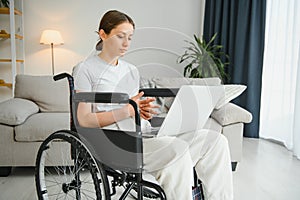 woman in a wheelchair works on the laptop PC in the home office with an assistance dog as a companion