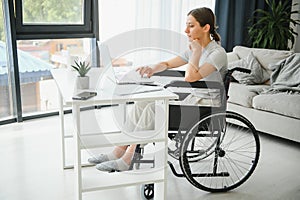 woman in a wheelchair works on the laptop PC in the home office with an assistance dog as a companion