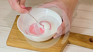 Woman whipped red color icing ream in the white bowl