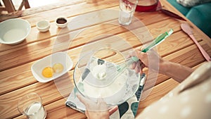 A woman whipping eggs whites with a whisk in a glass bowl and adding sugar