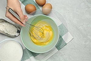 Woman whisking eggs in bowl at grey table, top view. Space for text