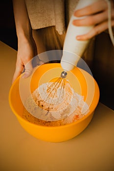 A woman is whisking flour and other ingredients in a bowl. The domestic baking and cooking. Homemade food