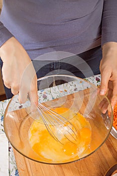 Woman whisks chicken eggs lying in a glass bowl with a kitchen whisk.