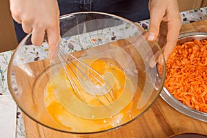 Woman whisks chicken eggs lying in a glass bowl with a kitchen whisk.