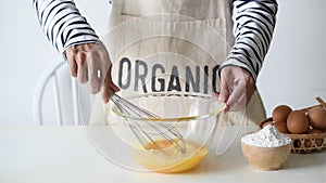 Woman whisks chicken eggs lying in a glass bowl with a kitchen whisk