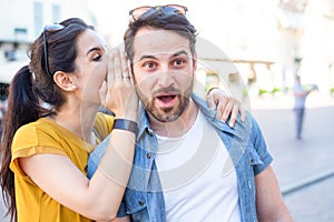 Woman is whispering a secret into his boyfriends ear photo