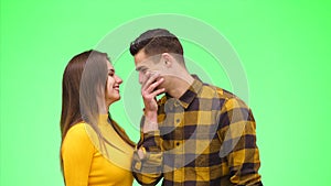 Woman is whispering a secret to her surprised young man on green background. Close up. Copy space. 4K.