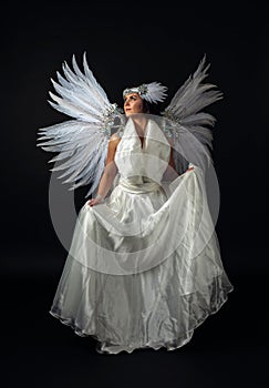 Woman in white angel costume with wings on a black background