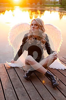 woman with white angel wings. wearing black leather clothes. fallen dark angel. demon. beast. girl in angel costume on