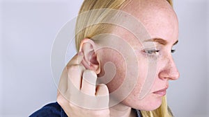 A woman on a white background shows her ear. The macro video shows the curl of the auricle, which has a tubercle. Plastic surgery