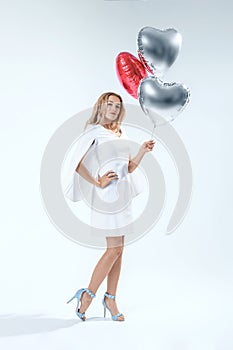 Woman on white backgroung holds red and silver balloons
