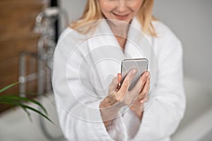 A woman in a white bath robe with a smartphone in her hands