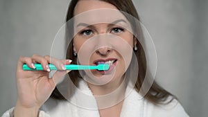 Woman in white bathrobe cleans her teeth with toothbrush and paste after shower.
