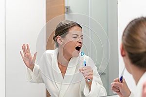 Woman in white bathrobe holding toothbrush, standing in bathroom