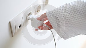 Woman in white bathrobe inserting plug into outlet at home with hand closeup