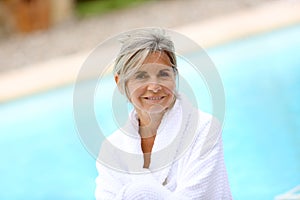 Woman with white bethrobe sitting near pool