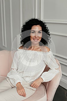 Woman in white blouse with african curls sits on sofa