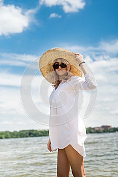 Woman in white blouse and straw hat resting on a hot summer day walking on  lake