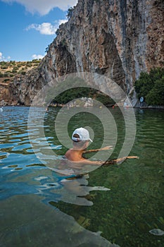 Woman in a white cap covered with fish peeling at the Voulagmeni thermal lake, Greece