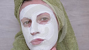 Woman in a White Clay Mask on Face and a Green Towel on Head. Close-up. 4K