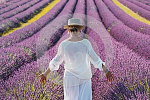 Woman with white clothes and hat walking in lavender violet field flowers. Female enjoy scenic travel destination. Outdoor leisure
