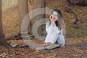 A woman in white clothes is resting after standing on sharp nails. Beautiful girl sits on the ground in the park next to