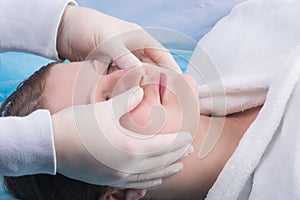 Woman, in a white coat, doing facial massage at Spa treatments, close-up