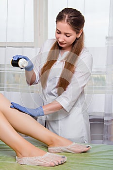 Woman in white coat, hair removal specialist at work in a beauty salon. Girl, a beauty salon worker waxes the client`s legs