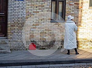 A woman in a white coat and white hat. The woman is standing with her back. Suitcase on the sidewalk. Waiting for a meeting