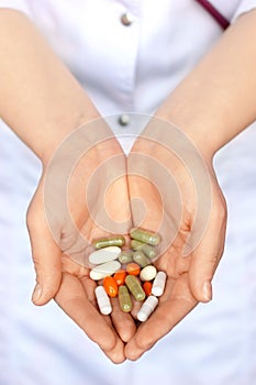 Woman in white coat holding a handful of pills in palms