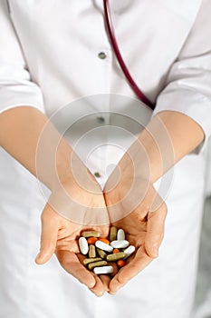 Woman in white coat holding a handful of pills in palms