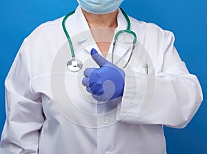 Woman in white coat, wearing blue medical latex gloves on her hands,showing like gesture with his  hand