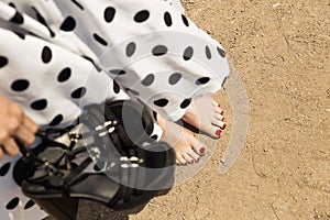woman in a white dotted dress holding her shoes, closeup barefoot