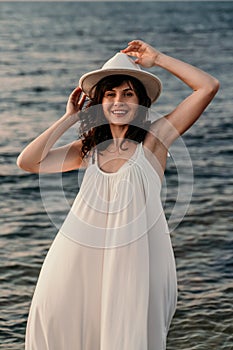 A woman in a white dress and hat is standing on the beach enjoying the sea. Happy summer holidays