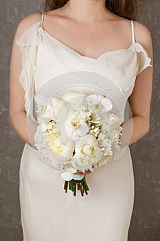 Woman in a white dress holding white bouquet with peonies, carna