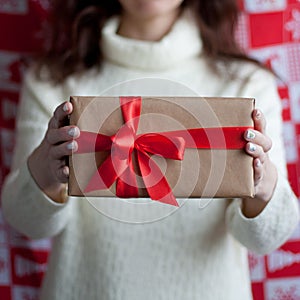 Woman in white dress holds a gift box wrapped in kraft paper and decorated with red ribbon with bow