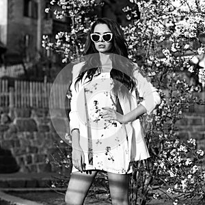 Woman in white dress and jacket posing against blooming shrub on background