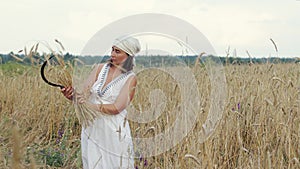 Woman in a white dress and kerchief knits a sheaf of wheat ears when harvesting grain crops