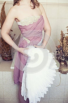 Woman in white dress with lilac belt and angel wing in hand