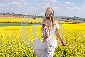 Woman in white dress looking out over fields of golden canola