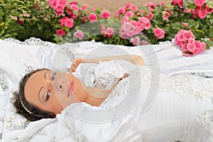 Woman in white dress lying on lawn among flowers