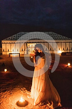 Woman in white dress, night near burning candle. Romantic evening in desert camp