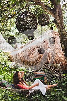 Woman in white dress relaxing in hanging hammock in Bali garden