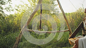 Woman in a white dress relaxing on a wooden swing in a lush forest at golden hour. Peaceful solitude and nature