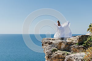 Woman in a white dress on the sea. Side view Young beautiful sensual woman in white long dress posing on a rock high