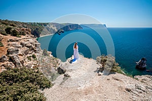 Woman in a white dress on the sea. Side view Young beautiful sensual woman in white long dress posing on a rock high