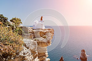 Woman in a white dress on the sea. Side view Young beautiful sensual woman in white long dress posing on a rock high